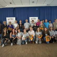 ein Gruppenfoto mit zwei  Roll-Ups, auf denen "Mit Dir" zu lesen ist