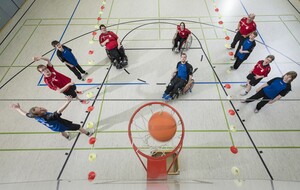 10 Jugendliche in roten und blauen Shirts untern Basketballkorb aus der Vogelperspektive