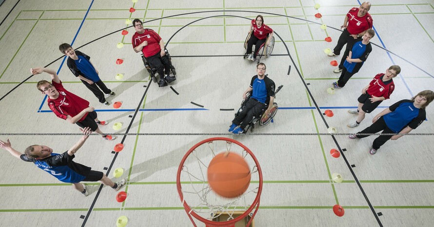 10 Jugendliche in roten und blauen Shirts untern Basketballkorb aus der Vogelperspektive