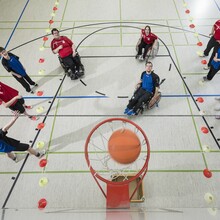 10 Jugendliche in roten und blauen Shirts untern Basketballkorb aus der Vogelperspektive