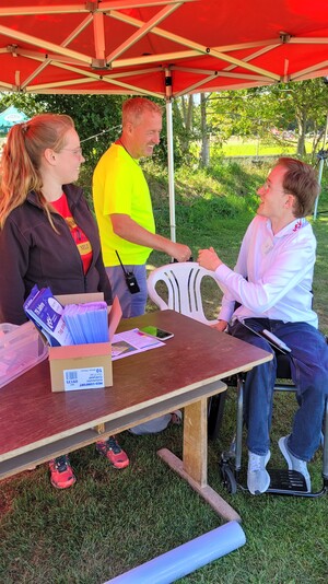 ein Team aus drei Personen an einem kleinen Stand im Schatten auf der Wiese