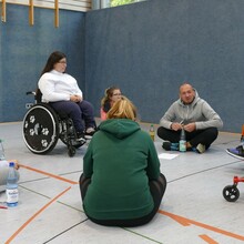 eine Gruppe von Sportlerinnen sitzt zum Teil im Rollstuhl, zum Teil auf dem Boden und diskutiert 
