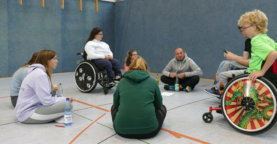 eine Gruppe von Sportlerinnen sitzt zum Teil im Rollstuhl, zum Teil auf dem Boden und diskutiert 