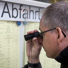 ein Mann mit Lupe versucht die Aushänge der Bahn zu lesen