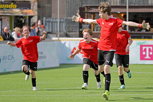 Vier Fußbaballspieler in roten Trikots laufen jubelnd über den Rasen