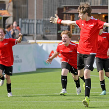 Vier Fußbaballspieler in roten Trikots laufen jubelnd über den Rasen