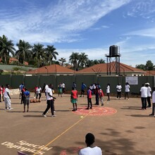 Ein Outdoor-Sportplatz mit Basketballkörben in Afrika und ca. 30 jungen Afrikaner*innen in unterschiedlichen Trikots