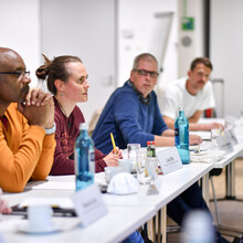 Vier Personen sitzen nebeneinander an einem Tisch und hören der einzigen Frau, die gerade spricht, aufmerksam zu. Foto: DOSB/Kai Peters