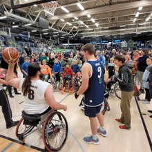 eine Gruppe von Kindern in Rollstühlen wartet darauf, dass ihnen ein Rollstuhl-Basketballspieler den Ball von der Grundlinie zuwirft
