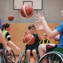 mehrere Rolsltuhlfahrer*innen mit mehreren Basketbällen in der Luft 