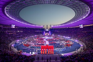 Blick von oben in ein volles Stadion in lila Licht, im Vordergrund ein Nachbau des Brandenburger Tors in rot